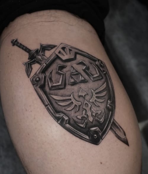 A black and grey realism tattoo of a shield with a sword on the thigh, featuring intricate details and shading — by Jian Liang, los angeles