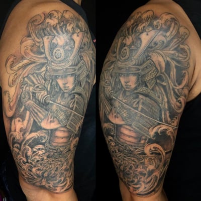 A bold black and grey tattoo of a samurai warrior with a sword on the upper arm, featuring detailed armor and flowing elements — by Sandra Price, los angeles