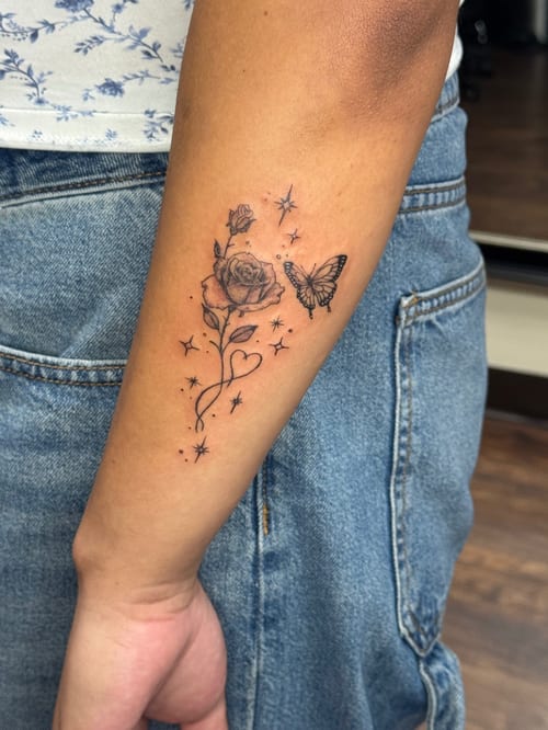 A delicate black and grey tattoo of a rose and butterfly on the forearm, featuring fine line work and minimalist details — by Sandra Price, los angeles