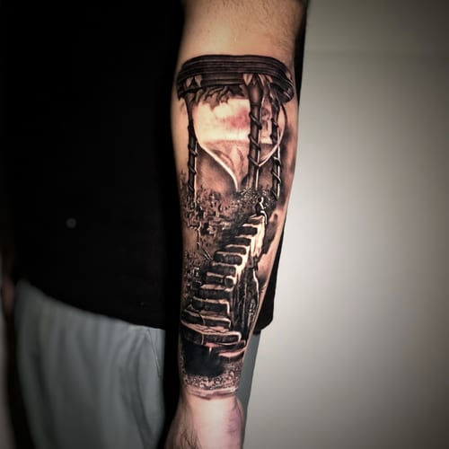 A black and grey realism tattoo on the forearm depicting a stairway leading up through a landscape with detailed shading — by Travis Ross, los angeles