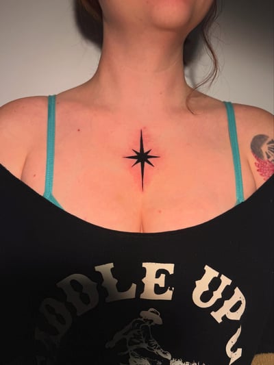 A minimalist black compass star tattoo on the chest, featuring clean lines and a simple design — by Shelby Bianco, los angeles