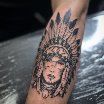 A bold blackwork Native American portrait tattoo on the forearm featuring a feather headdress — by Maddie Ramirez, los angeles