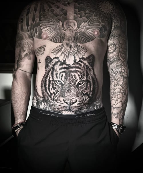 A detailed black and grey realism tattoo of a tiger's face on the stomach, accompanied by a bird and script elements — by INKEDBy_G, los angeles