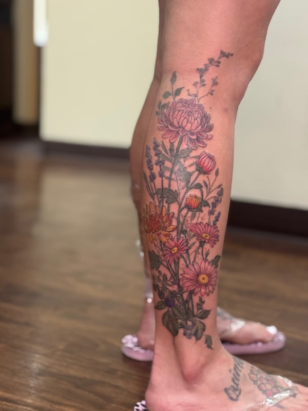 A colorful floral bouquet tattoo on the calf featuring various flowers in a delicate and romantic style — by Sandra Price, ventura, ca