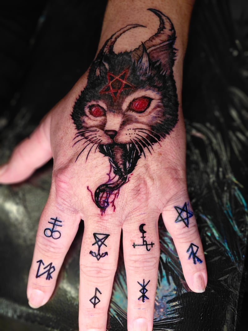 dark occult blackwork tattoo of a horned demon cat with a red pentagram on the back of the hand by anoetic.designs, a blackwork tattoo artist in los angeles