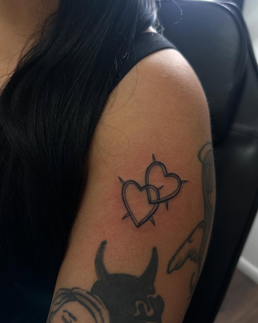 A bold blackwork tattoo of interlocking hearts with spikes on the upper arm — by Maddie Ramirez, los angeles