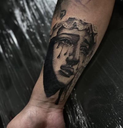 A black and grey tattoo of a crying woman's face on the forearm, done in blackwork and fine line style — by Maddie Ramirez, los angeles