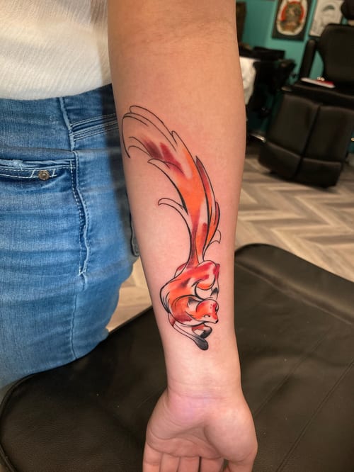A colorful illustrative tattoo of a stylized orange animal on the forearm, featuring bold outlines and vibrant shading — by Josue Bravo, los angeles