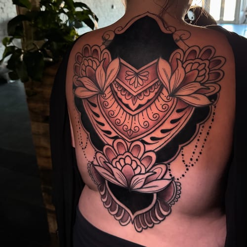 An ornamental black and grey tattoo on the back featuring intricate floral patterns and bold blackwork elements — by Travis Ross, los angeles