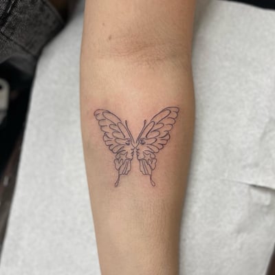 A minimal linework tattoo of a butterfly with faces on the forearm, featuring a delicate and simple design — by Sandra Price, los angeles