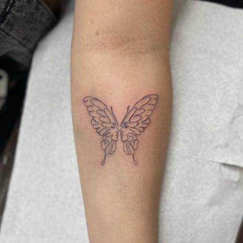 A minimal linework tattoo of a butterfly with faces on the forearm, featuring a delicate and simple design — by Sandra Price, los angeles