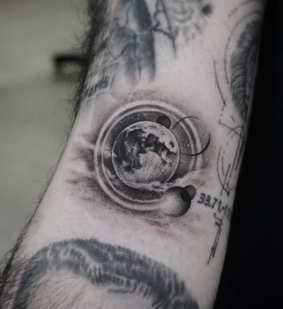 A black and grey surrealistic tattoo of celestial bodies, including a detailed moon and planets, on the forearm — by Jian Liang, los angeles