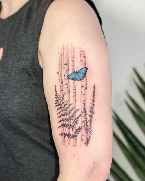 A delicate tattoo of a blue butterfly with ferns and birch trees on the upper arm, done in fine line style with mixed color and black ink — by Melanie Benoit, los angeles