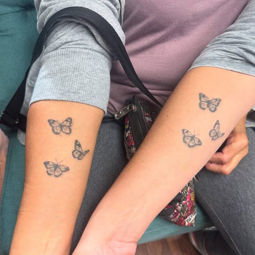 A delicate black and grey fine line butterfly tattoo on the forearm, featuring multiple small butterflies — by Sandra Price, los angeles
