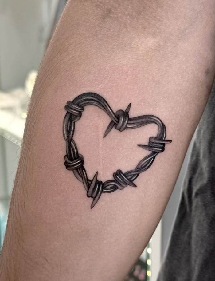 A black and grey minimalist tattoo of a heart made from barbed wire on the arm — by otaybeatdown, los angeles