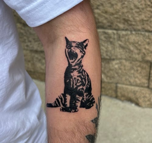 A minimalist blackwork tattoo of a yawning cat on the forearm, featuring bold lines and simple shading — by velvet devil, los angeles