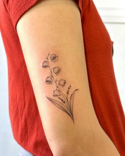 A delicate fine line tattoo of a lily of the valley on the arm, featuring detailed floral elements in black and grey — by Melanie Benoit, los angeles