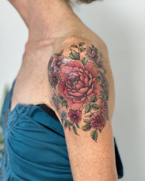 A colorful floral bouquet tattoo on the shoulder featuring roses and other flowers in a delicate and romantic style — by Melanie Benoit, los angeles
