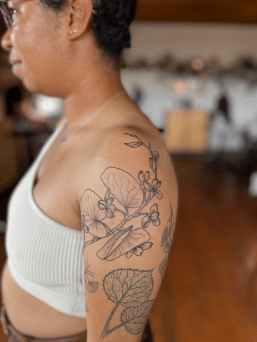 A black and grey fine line tattoo of flowers and leaves on the upper arm, featuring delicate linework and botanical elements — by Dylan Aiello, los angeles