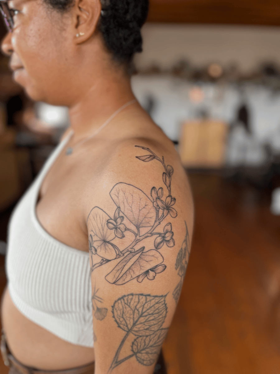A black and grey fine line tattoo of flowers and leaves on the upper arm, featuring delicate linework and botanical elements — by Dylan Aiello, los angeles