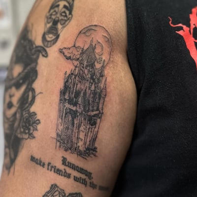 A detailed blackwork tattoo of a gothic castle with a moon on the upper arm, featuring fine line work and a dark, delicate style — by Maddie Ramirez, los angeles