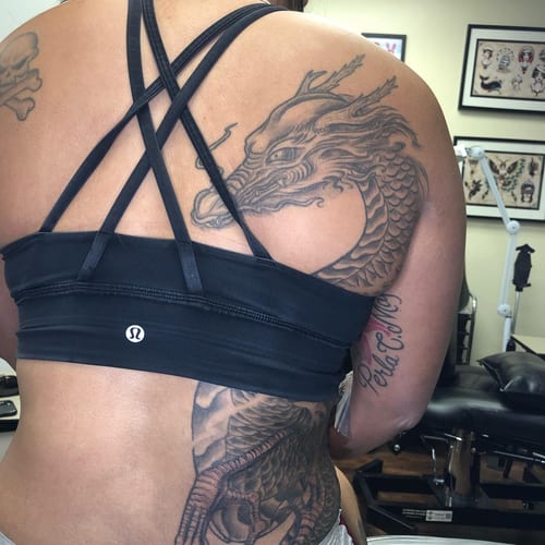 A bold black and grey Japanese dragon tattoo covering the upper back with intricate scale details — by Sandra Price, los angeles
