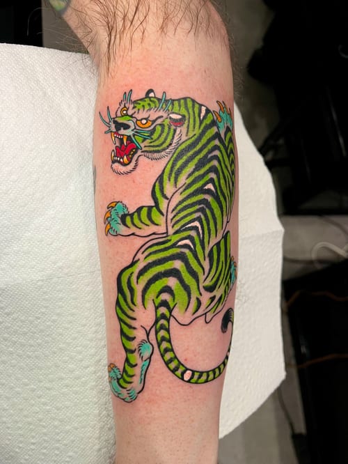 A colorful Japanese-style tiger tattoo on the forearm, featuring bold lines and vibrant green and yellow hues — by Megan Rose, los angeles