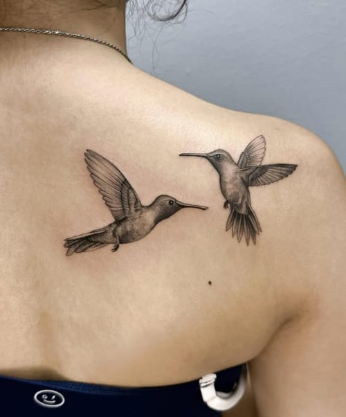 A black and grey realism tattoo of two hummingbirds on the upper back, featuring detailed shading and lifelike depiction — by otaybeatdown, los angeles