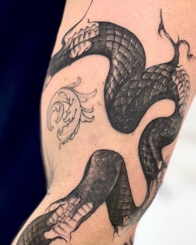 A black and grey tattoo of a snake wrapping around the arm, featuring bold blackwork with detailed scales — by otaybeatdown, los angeles
