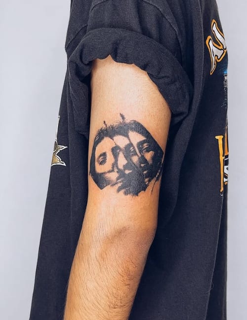 A black and grey portrait tattoo on the upper arm featuring three faces with detailed shading — by Level tattoo, los angeles