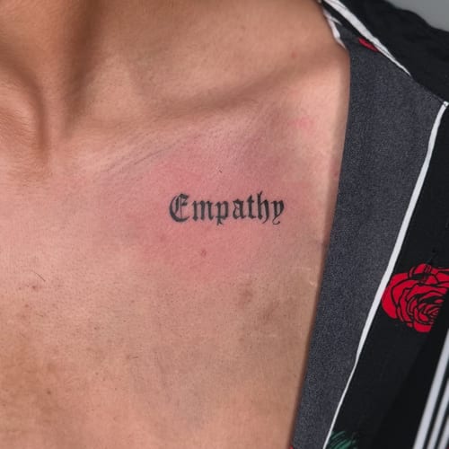 A minimal black script tattoo on the chest featuring the word 'Empathy' in a classic font — by zealous, los angeles