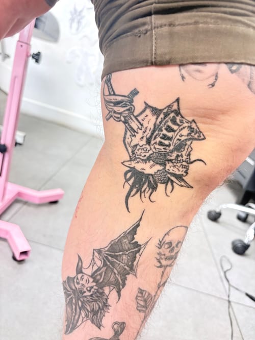 A black and grey illustrative tattoo on the thigh featuring a skull and bat with bold outlines and shading — by Hannah , los angeles