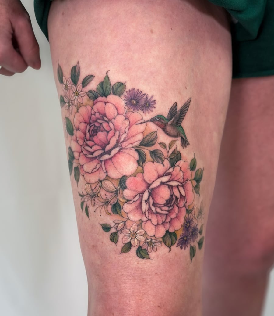 A colorful tattoo of a hummingbird hovering near flowers on the thigh, done in a realistic and botanical style — by Melanie Benoit, los angeles