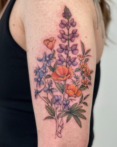 A colorful floral bouquet tattoo on the upper arm featuring various flowers in a delicate and romantic style — by Melanie Benoit, los angeles