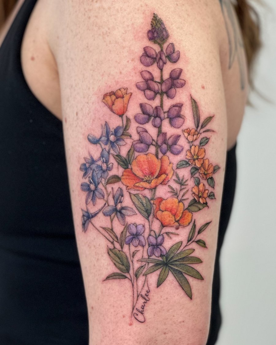 A colorful floral bouquet tattoo on the upper arm featuring various flowers in a delicate and romantic style — by Melanie Benoit, los angeles