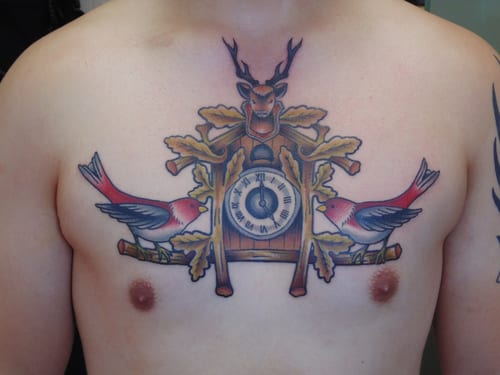 A colorful traditional cuckoo clock tattoo on the chest with birds and bold outlines — by Samuel Connelly, los angeles
