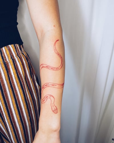 A minimalist red linework snake tattoo on the forearm, featuring a simple and elegant design — by Level tattoo, los angeles