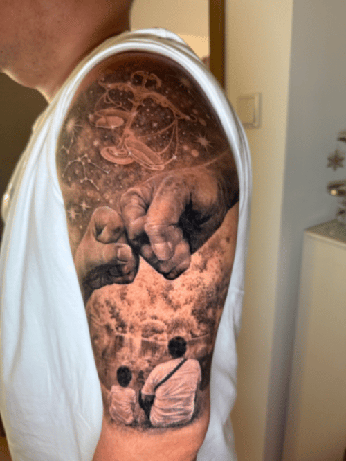 A black and grey realism tattoo on the upper arm depicting a celestial scene above two people sitting together, with a detailed depiction of hands in the foreground — by 钟逸政, los angeles