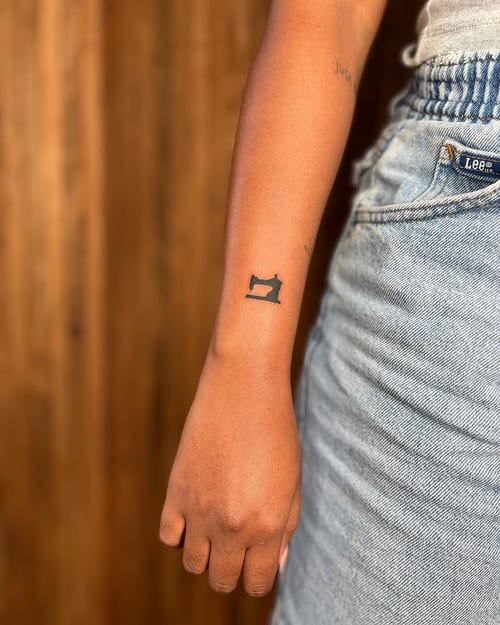 A minimalist blackwork sewing machine tattoo on the forearm, featuring a simple and clean design — by Dylan Aiello, los angeles