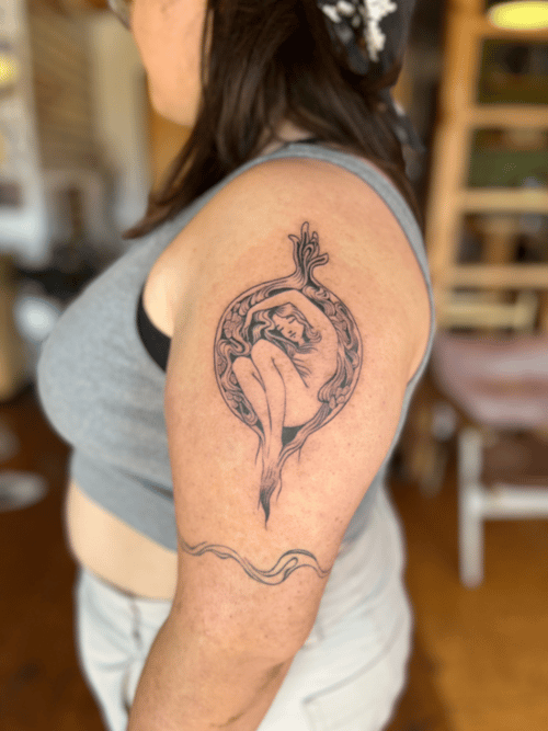 A black and grey linework tattoo of a woman curled up within a circular design on the upper arm, featuring intricate line details and a flowing pattern — by Dylan Aiello, los angeles
