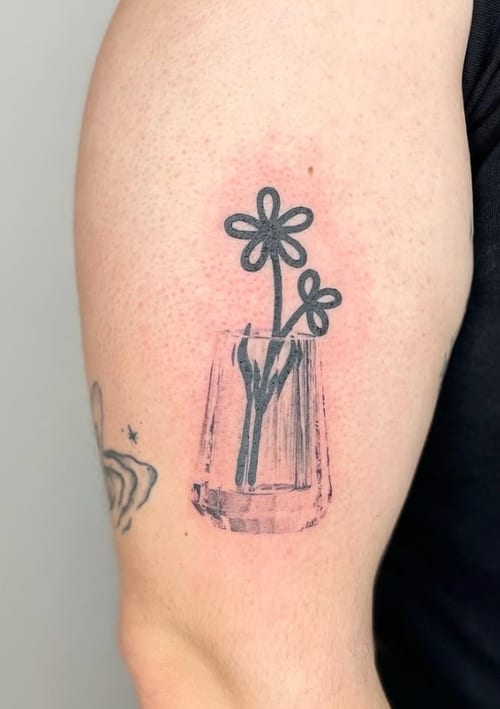 A minimalist black and grey tattoo of simple line-drawn flowers in a vase on the upper arm — by Level tattoo, los angeles