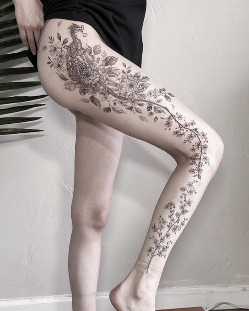 A delicate black and grey tattoo of a dragon intertwined with flowers on the leg, featuring fine line details and ornate floral designs — by Melanie Benoit, los angeles