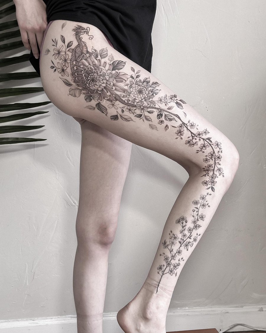 A delicate black and grey tattoo of a dragon intertwined with flowers on the leg, featuring fine line details and ornate floral designs — by Melanie Benoit, los angeles