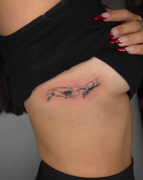 A fine line black and grey tattoo on the rib depicting two hands reaching towards each other with subtle shading — by ashynucklestattoo, los angeles