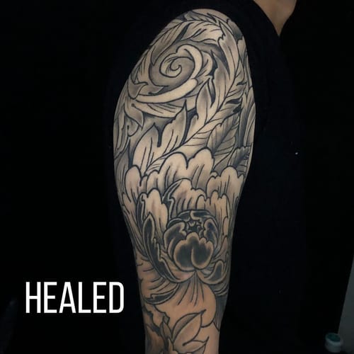 A black and grey Japanese-style floral tattoo on the upper arm with intricate leaf and petal details — by Sandra Price, los angeles