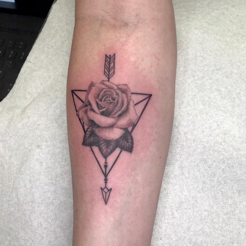 A black and grey rose tattoo with geometric elements on the forearm, featuring clean lines and delicate shading — by Sandra Price, los angeles