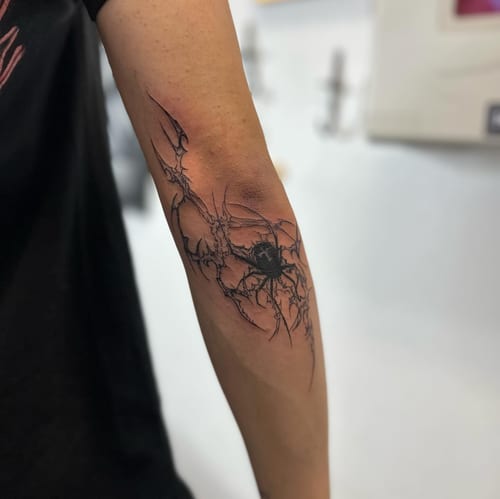 A dark blackwork tattoo of a spider with an abstract web on the forearm — by Maddie Ramirez, los angeles
