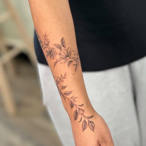 A delicate black and grey floral arrangement on the forearm, featuring fine line botanical details — by Melanie Benoit, los angeles