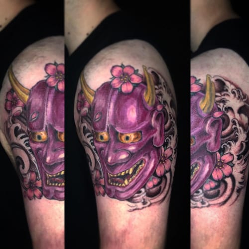 A colorful Japanese hannya mask tattoo on the upper arm, featuring bold colors and floral accents — by Sandra Price, los angeles