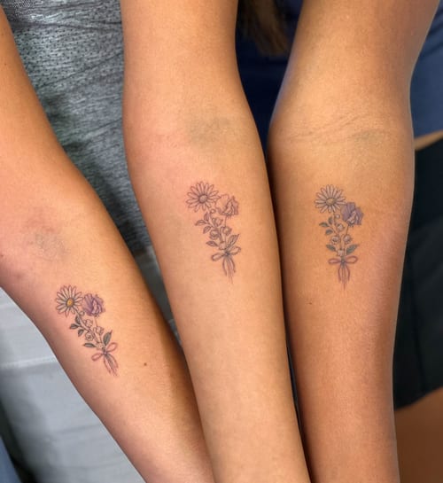 A delicate fine line flower bouquet tattoo on the forearm with minimalist style and subtle color accents — by Melanie Benoit, los angeles